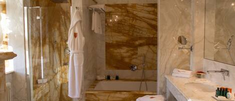 A modern bathroom with a glass-enclosed shower, a marble-tiled wall, a bathtub, and a vanity with toiletries.