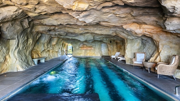 Uma piscina interior com teto assemelhado a uma gruta rochosa, rodeada por espreguiçadeiras.