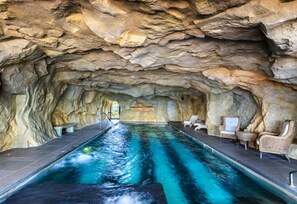 Una piscina interior con techo que simula una cueva rocosa, rodeada de sillones de descanso.