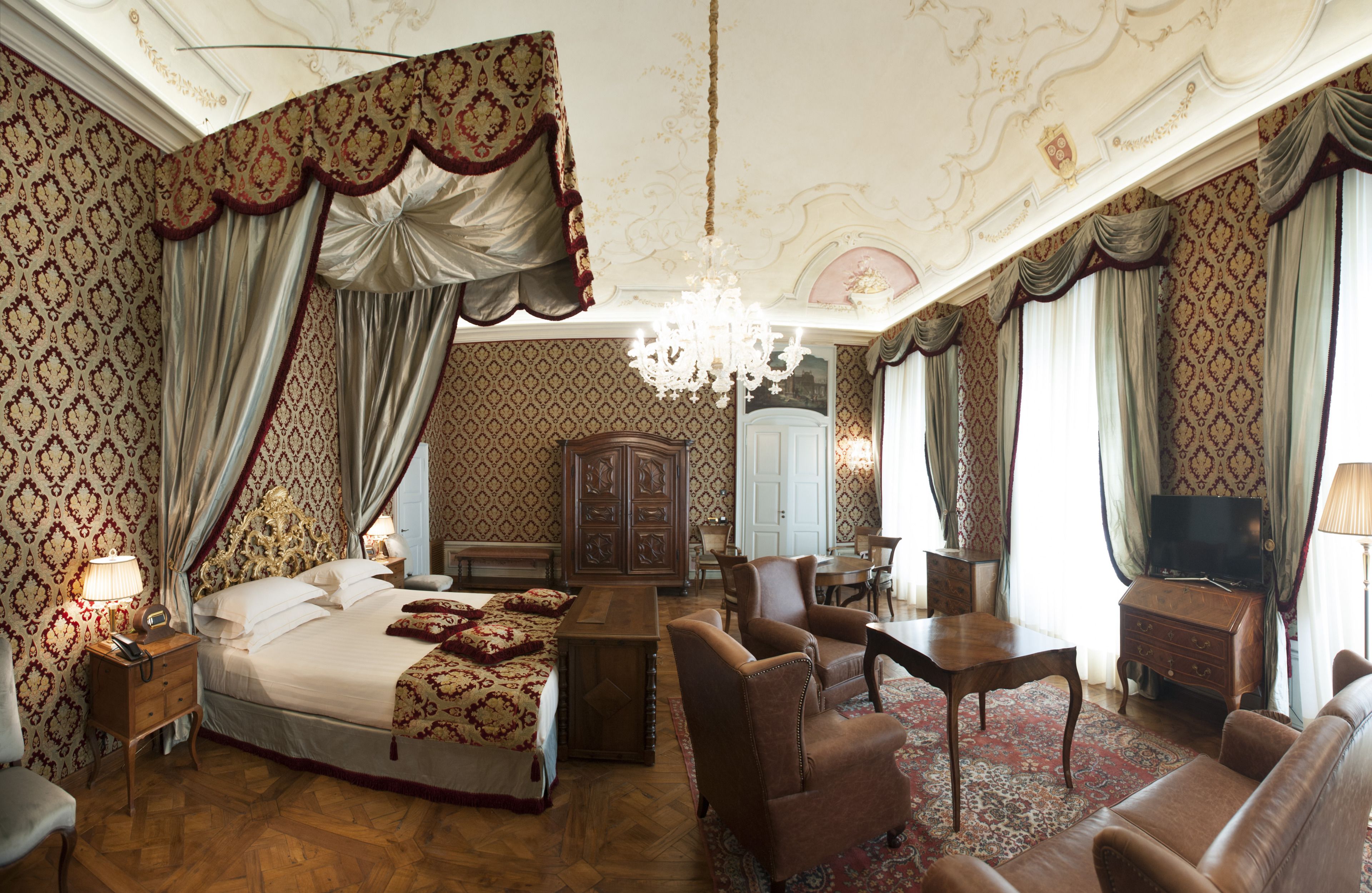 Une chambre luxueuse dotée d’un grand lit, d’une armoire en bois, d’une télévision et d’un coin salon avec un canapé et des fauteuils.