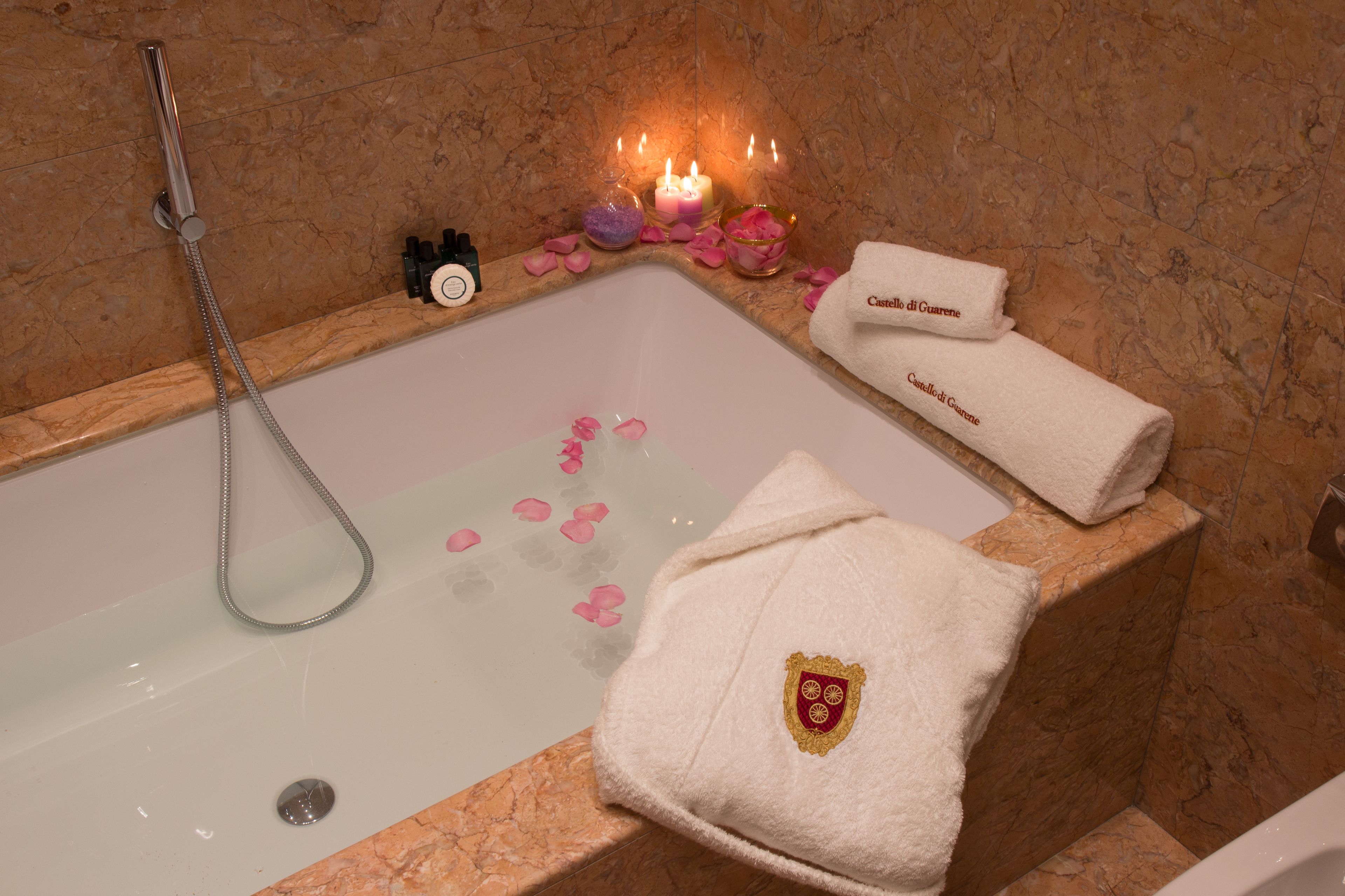 Una vasca da bagno con petali di rosa, candele e un asciugamano con uno stemma.