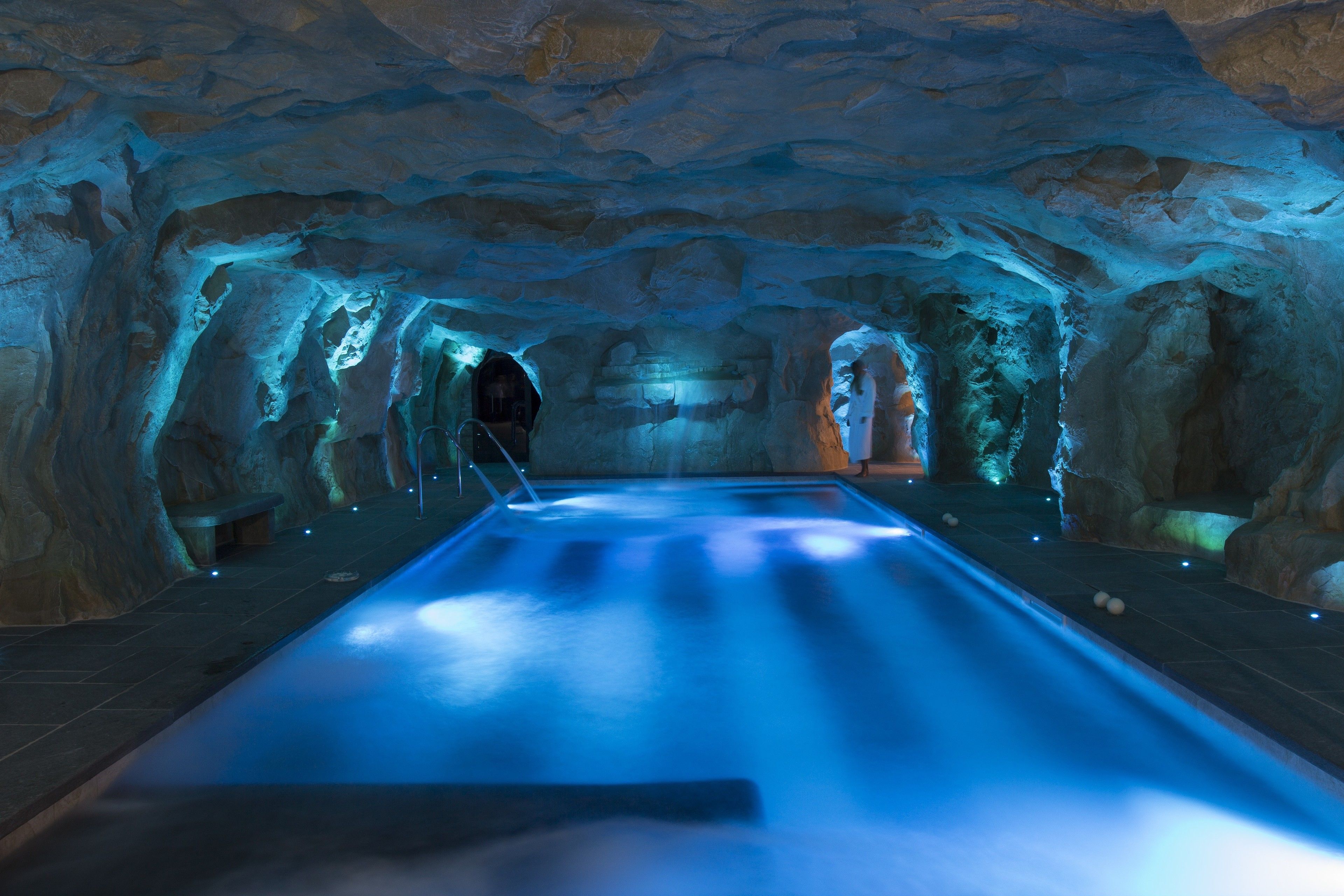 An indoor swimming pool with a stone wall backdrop and a bench.