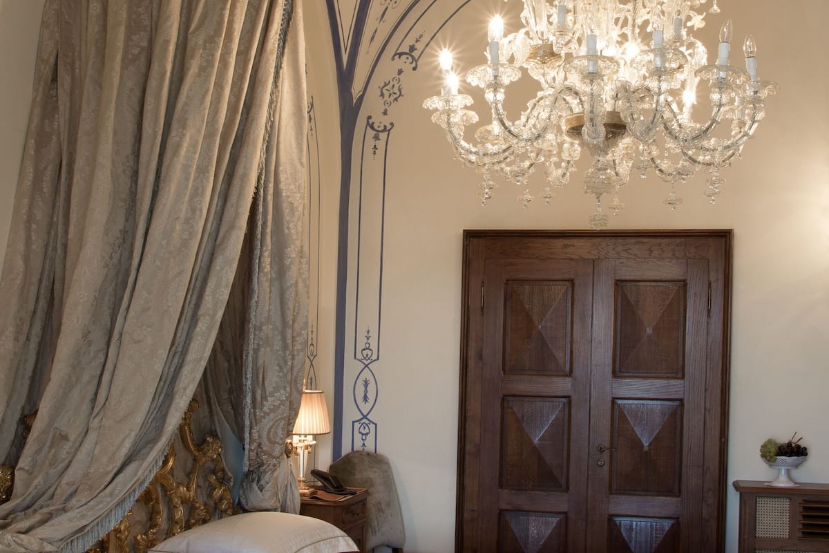 Ein Schlafzimmer mit einem Bett, einer Kristallleuchter, einer Holztür und einer Wand mit dekorativen Mustern.