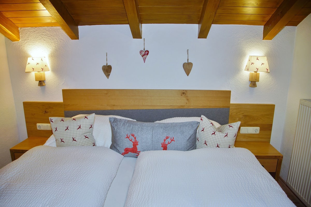A neatly made bed with a wooden headboard, two bedside tables with lamps, and decorative wall sconces.
