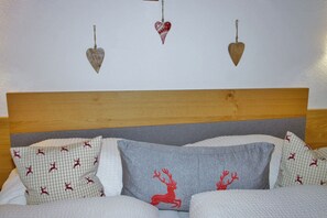 Une chambre à coucher avec une tête de lit en bois, du linge de lit blanc et des coussins décoratifs ornés de motifs de rennes et de cœurs.