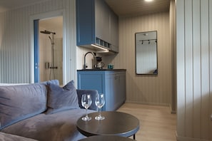 A modern kitchen with blue cabinets, a round table with two wine glasses, and a grey sofa.