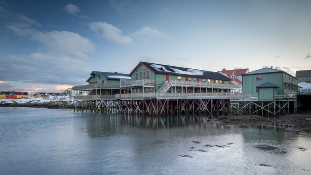 Un bâtiment situé au bord de l’eau, doté d’une terrasse en bois qui s’étend sur l’eau, et comprenant plusieurs niveaux et balcons.