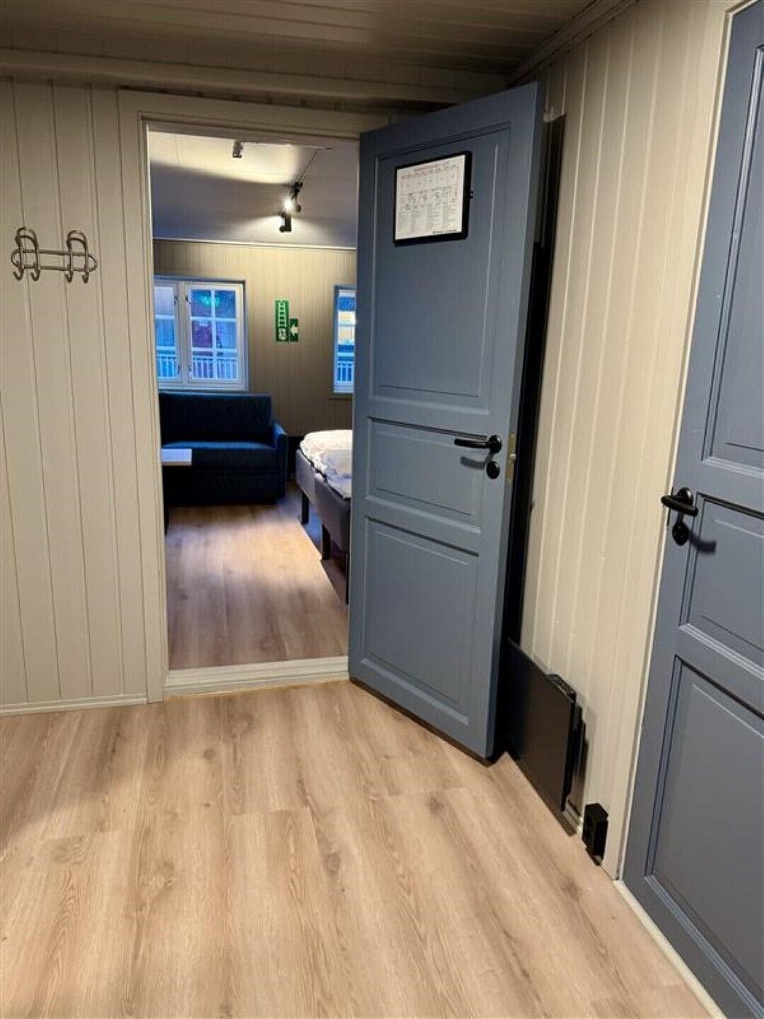 A hallway with a wooden floor leading to a room with a bed and a window.