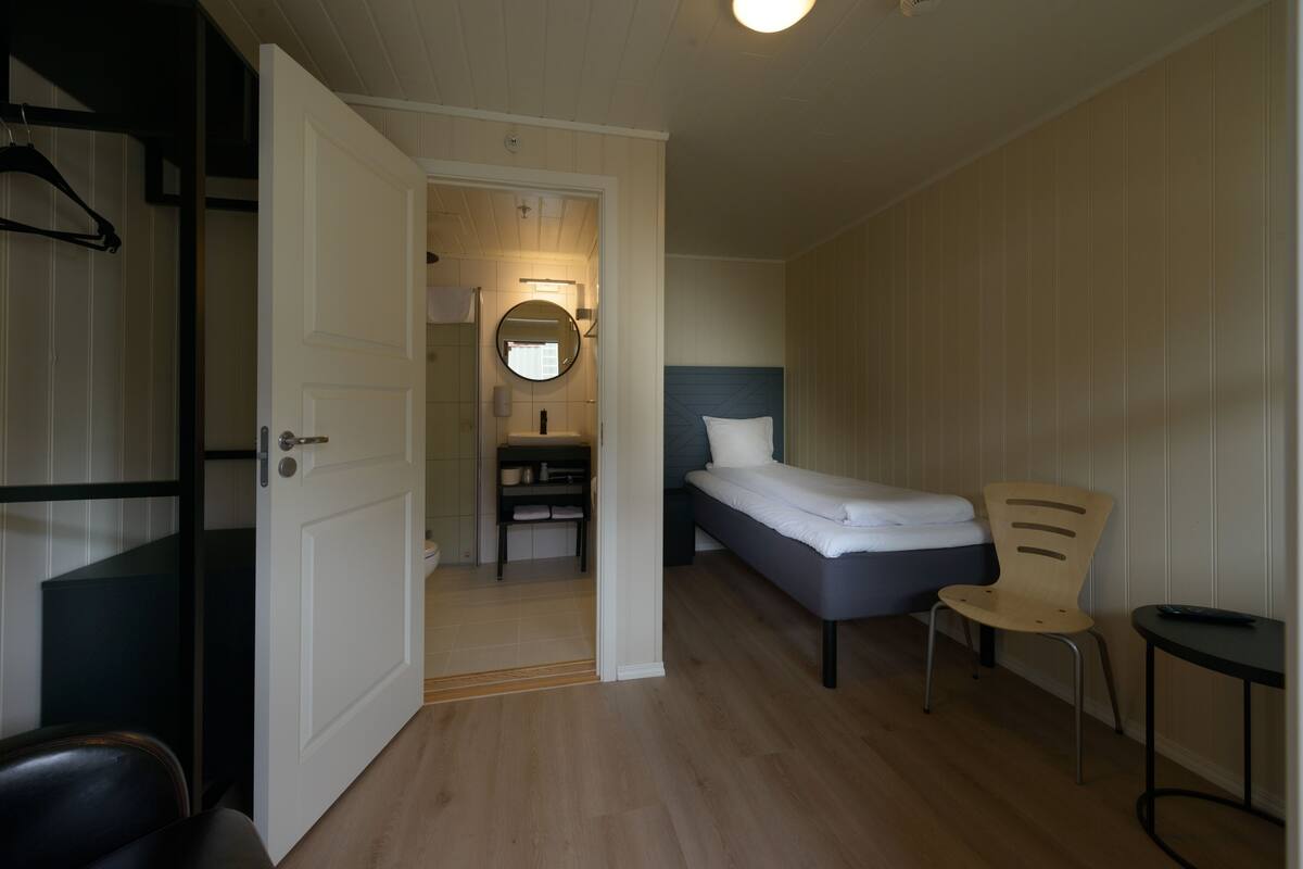 Quarto com cama, cadeira, mesa, espelho e porta para um banheiro.