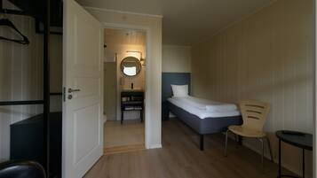 Un dormitorio con una cama, una silla, una mesita pequeña y un baño a la vista a través de una puerta abierta.