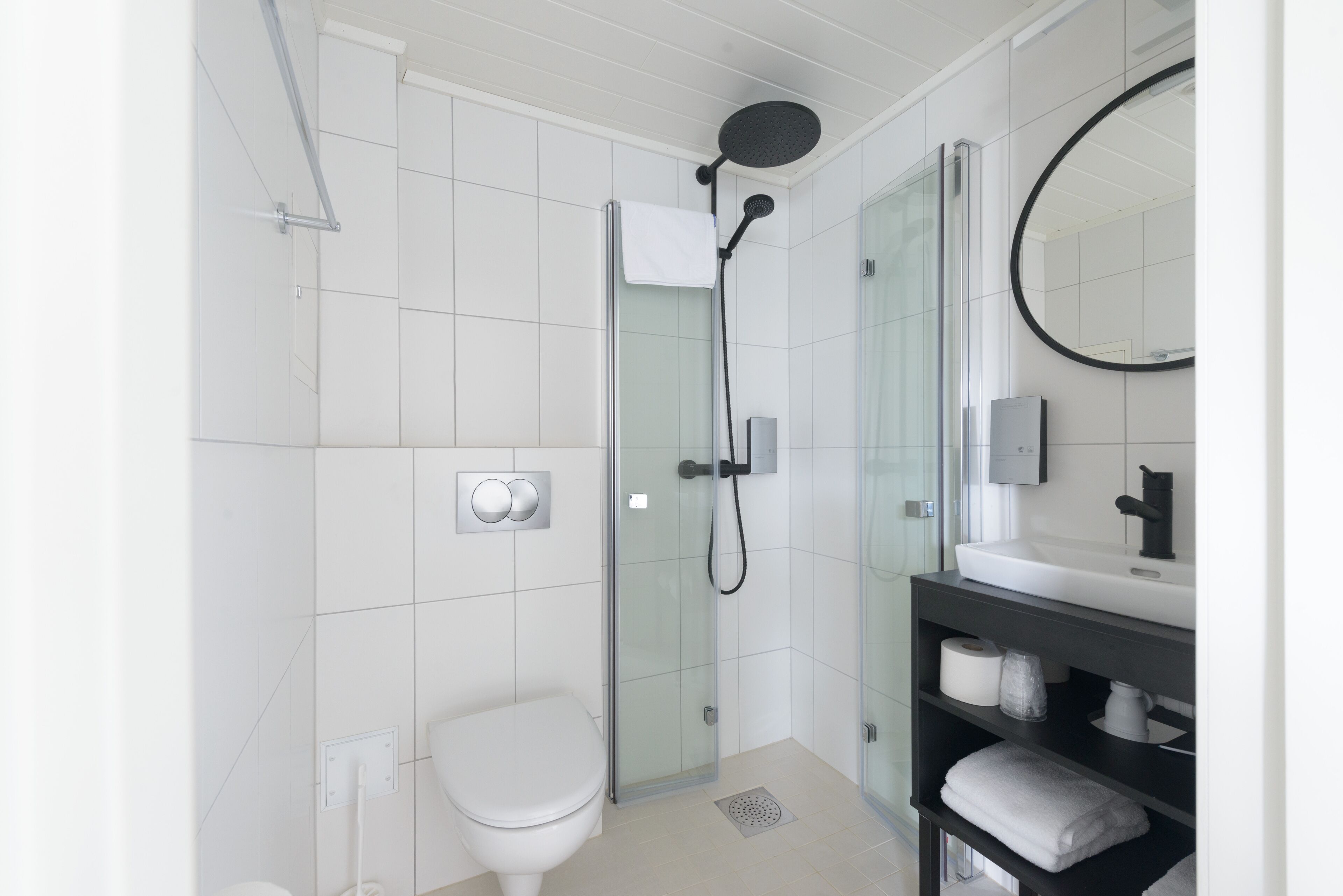 Ein modernes Badezimmer mit einer Duschkabine aus Glas, einer weißen Toilette und einem dunklen Holzwaschtisch mit Spiegel.