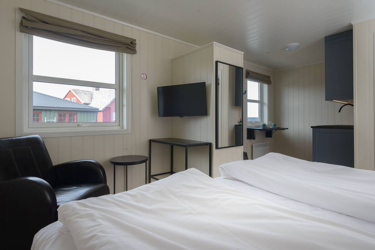 Quarto de hotel com duas camas, televisão, escrivaninha, cadeira e janela com vista para edifícios.