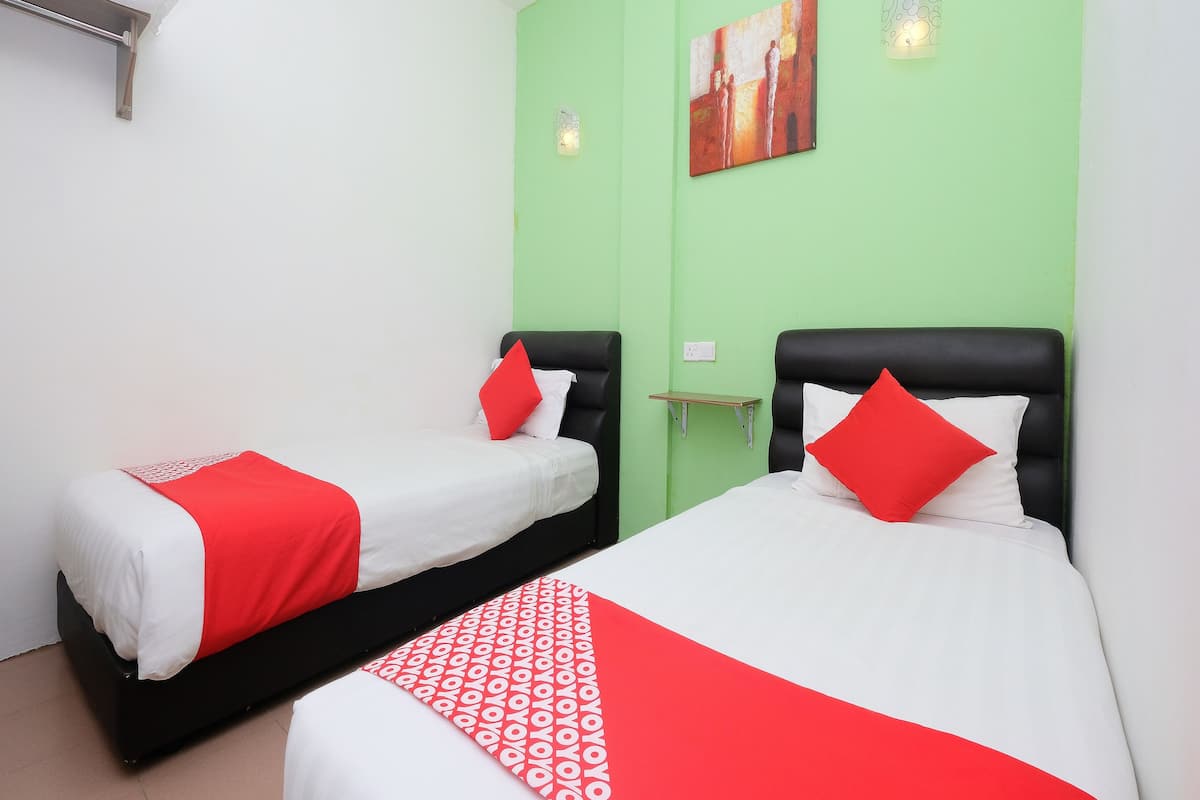 Habitación de hotel con dos camas, cada una con cabecero negro y ropa de cama blanca y roja. Una pared de acento verde y un cuadro sobre las camas.
