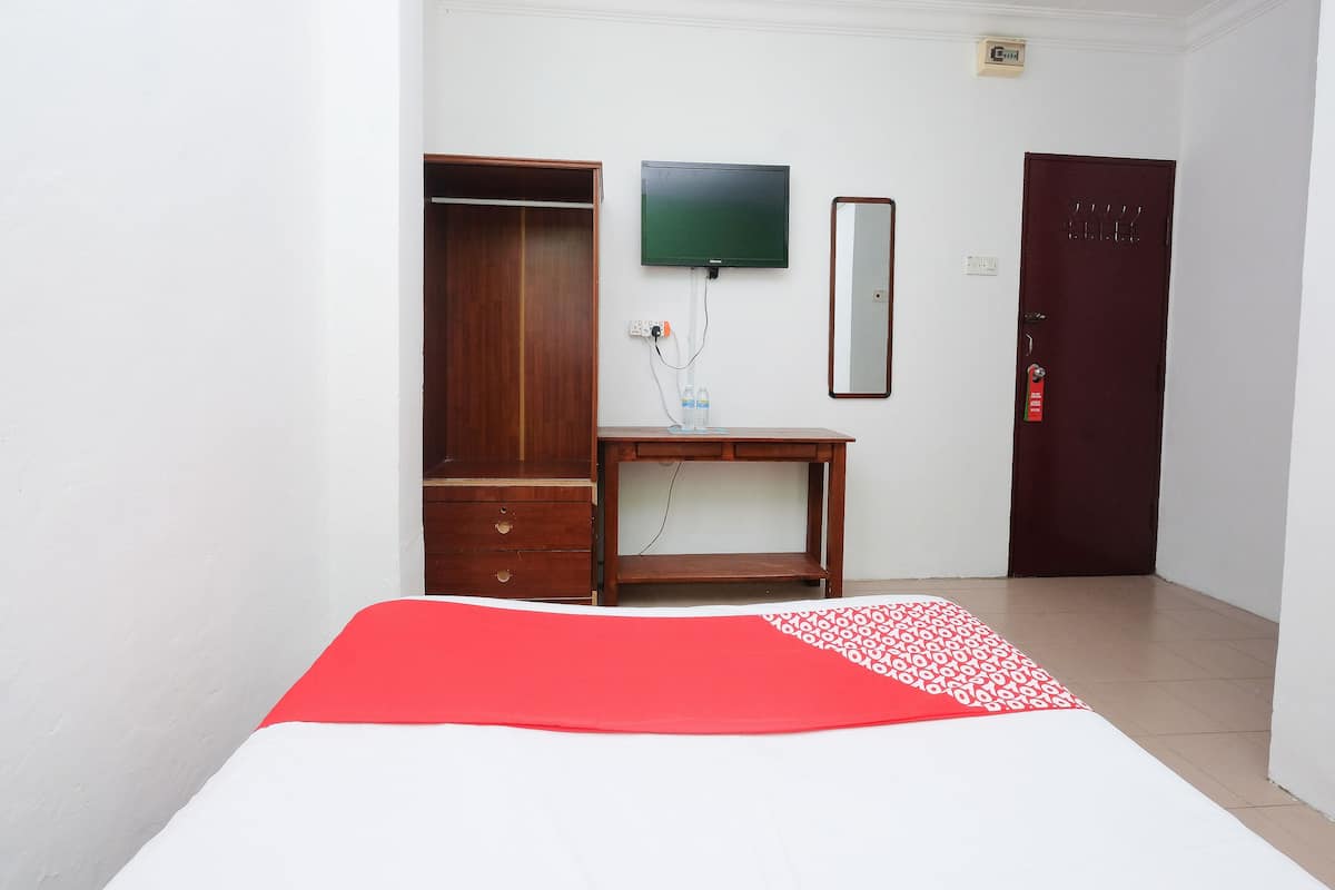 Habitación de hotel con cama, armario de madera, escritorio con espejo, televisor y puerta.