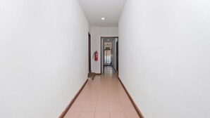 A long, narrow hallway with white walls and a tiled floor. A fire extinguisher is mounted on the wall. - OYO 850 Gold Star Hotel (Chukai)