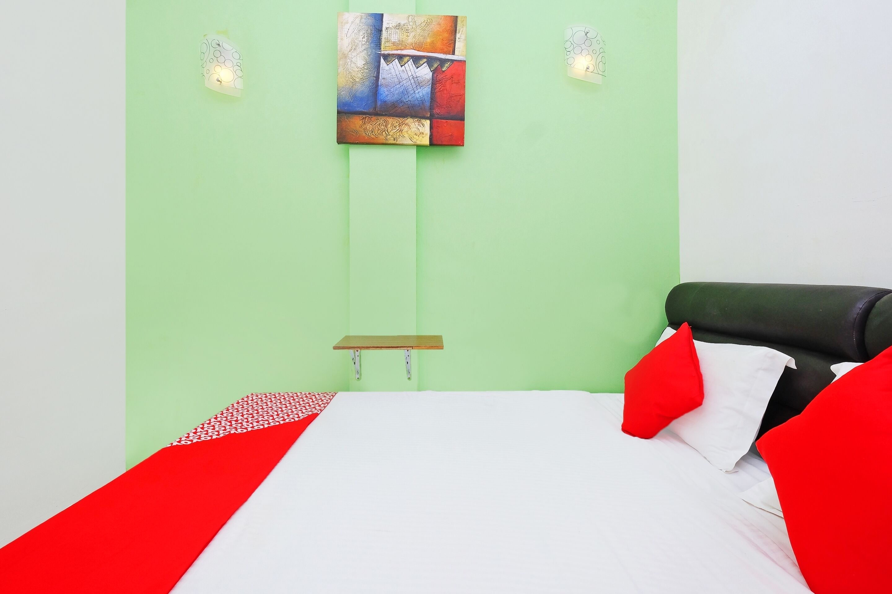 A bed with red and white bedding, a green wall, and a painting above the bed.