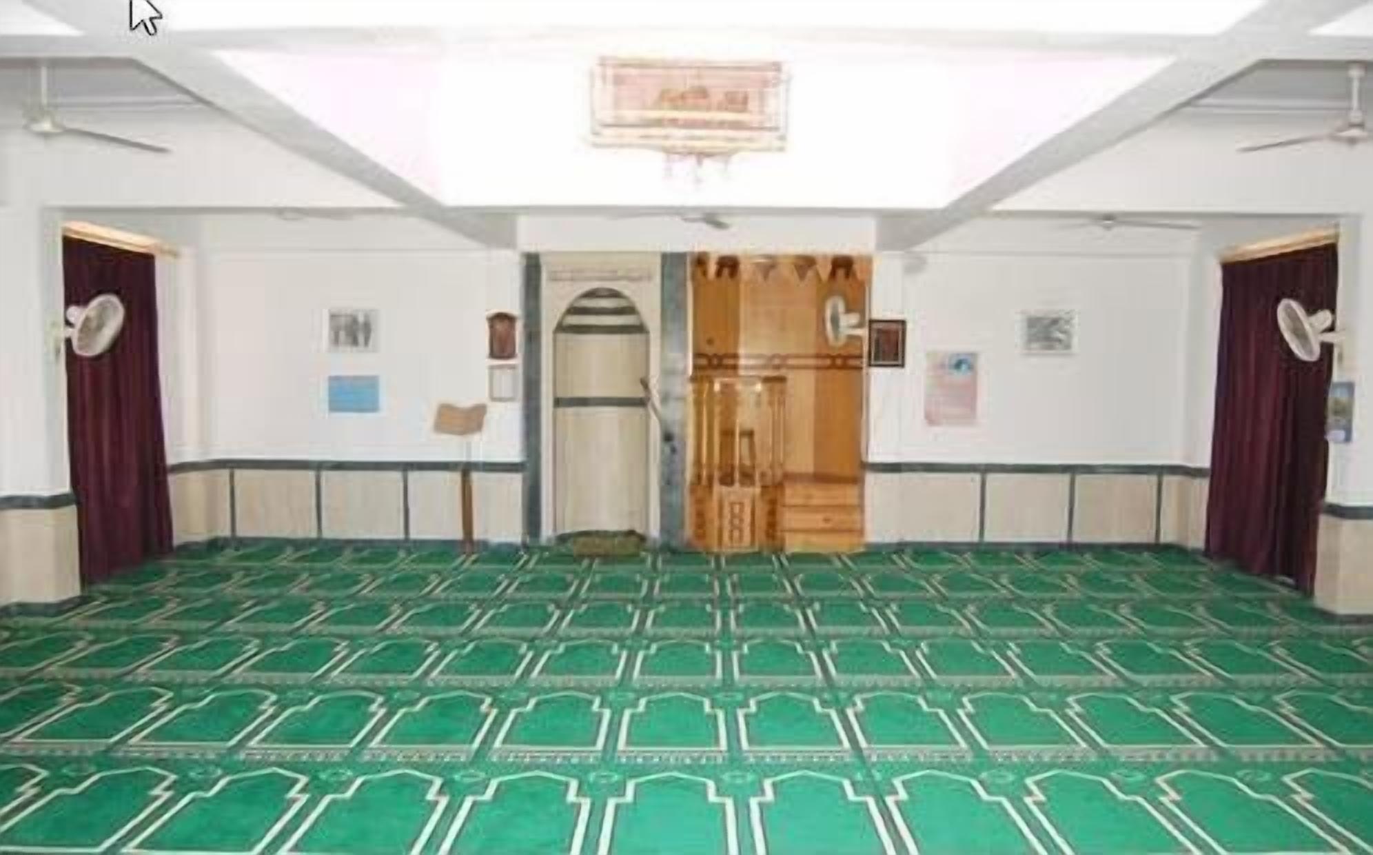A large room with a green patterned carpet, white walls, and a wooden door.