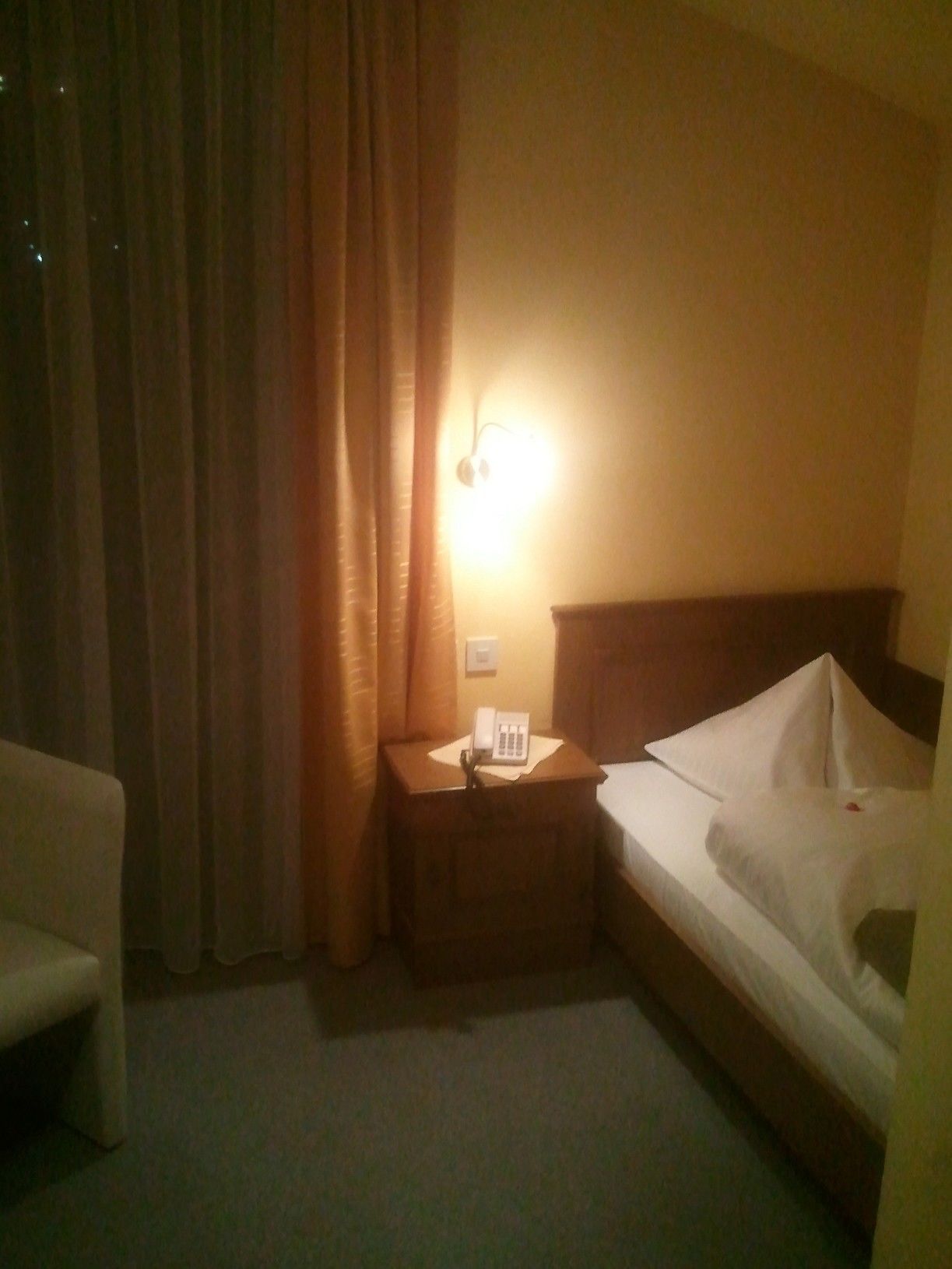 Een hotelkamer met een bed, een nachtkastje met een telefoon, een lamp en een stoel.