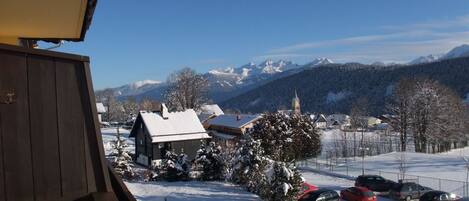A snowy mountain village with a church, residential buildings, and parked cars.