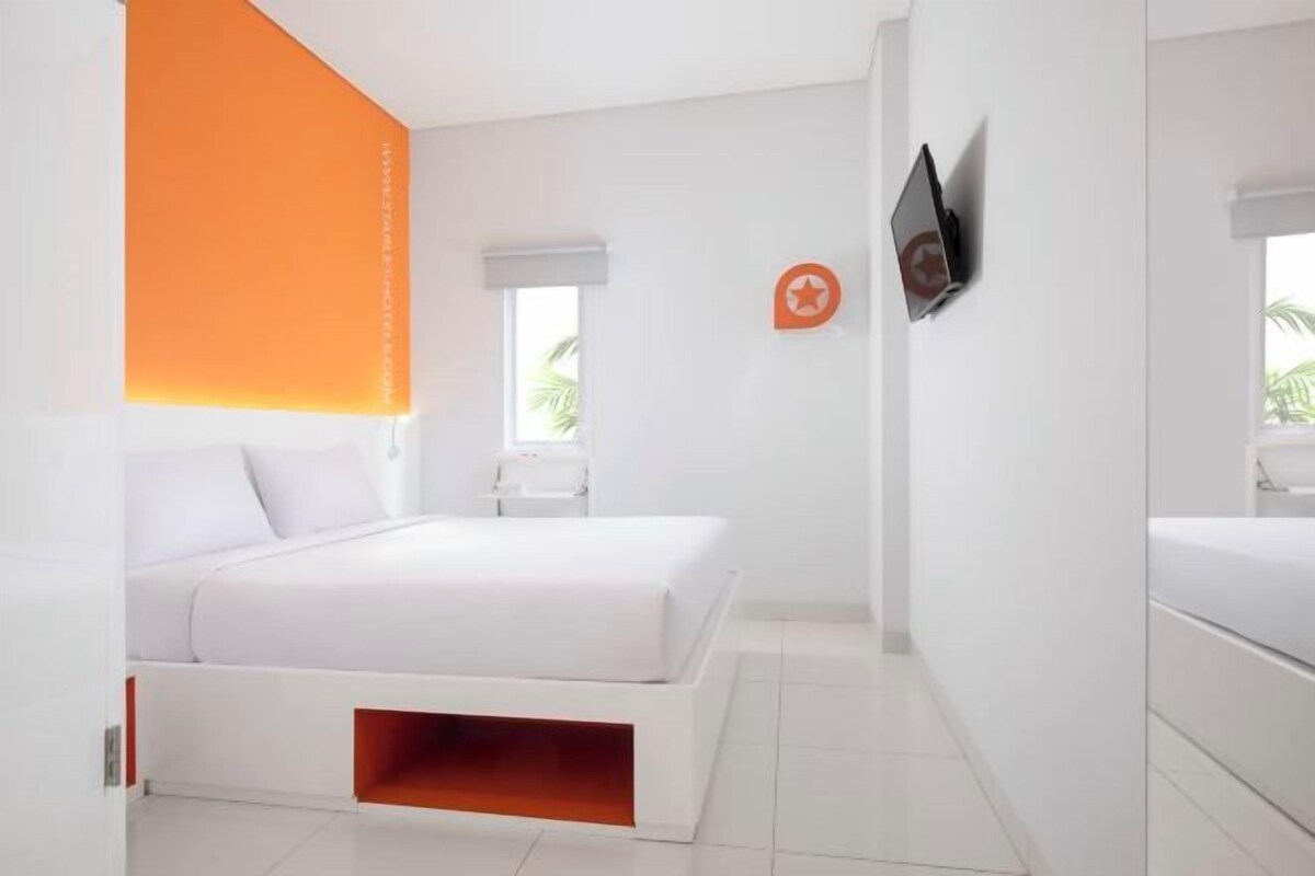 A modern hotel room with a bed, a TV mounted on the wall, and a window with a view of palm trees.