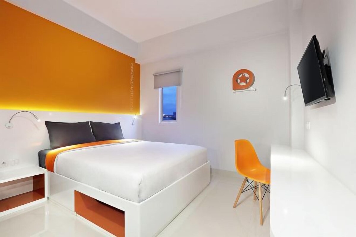 A modern bedroom with a bed, a chair, a TV, and a window.