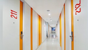 A modern hotel corridor with white walls and orange accents, featuring numbered doors and a clean, polished floor. - Starlet Hotel Serpong (South Tangerang)