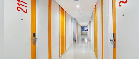Un pasillo moderno de hotel con paredes blancas y detalles en naranja, con puertas numeradas y un suelo limpio y pulido.