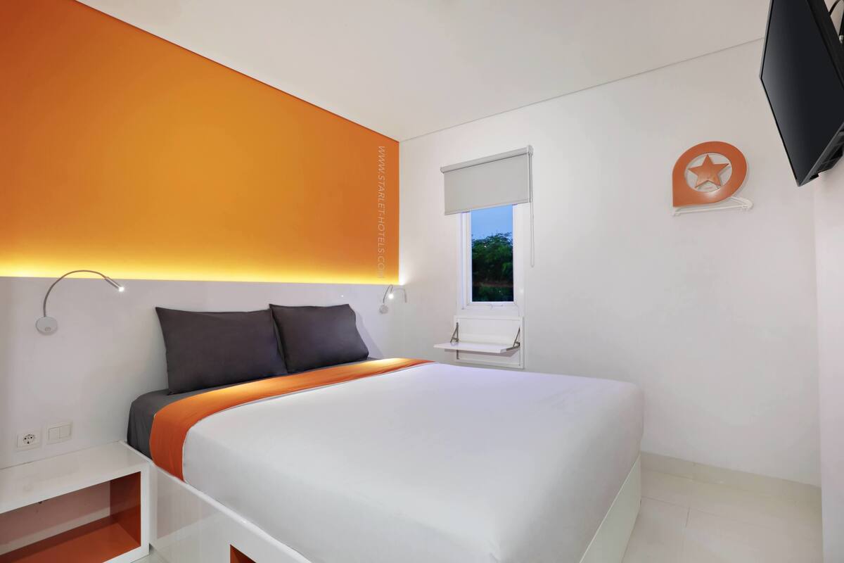A modern bedroom with a bed, bedside table, and a TV mounted on the wall.