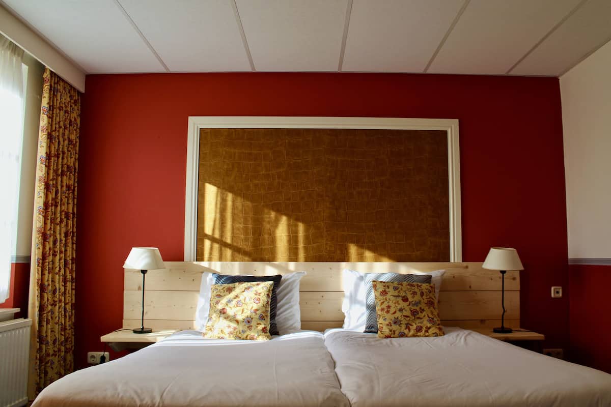 Una cama doble con almohadas estampadas, un cabecero de madera y dos lámparas de noche.