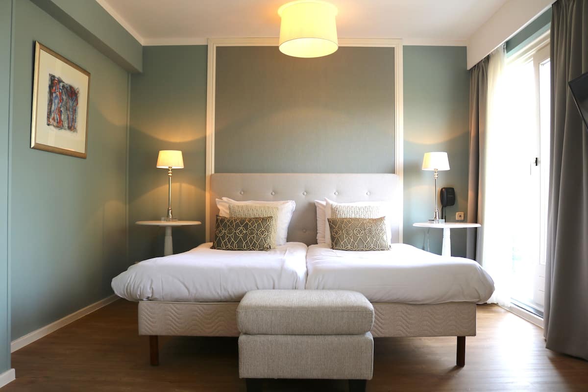 Una cama grande con cabecera, dos mesitas de noche con lámparas, un banco y un cuadro enmarcado en la pared.