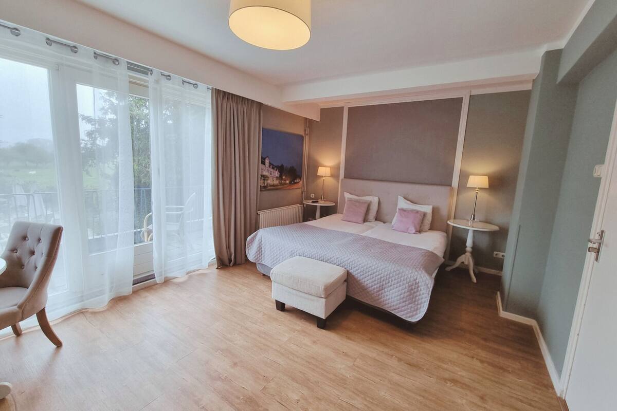 Un dormitorio con una cama grande, una silla, vistas al exterior y una lámpara en una mesita de noche.