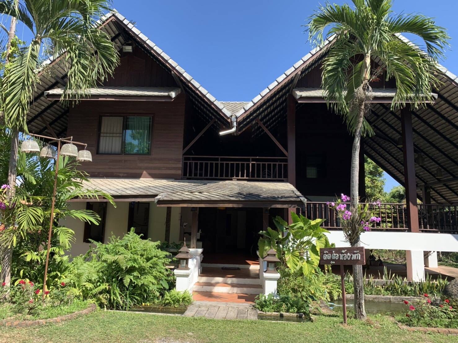 A two-story building with a sloped roof, surrounded by lush greenery and palm trees.