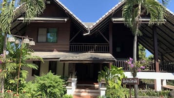 A two-story building with a sloped roof, surrounded by lush greenery and palm trees.