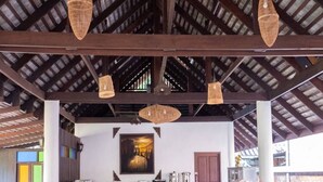 Un comedor interior con mesas y sillas de madera, piso de baldosas y lámparas colgantes de tejido.