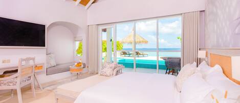 A spacious bedroom with a large bed, a desk, and a view of a swimming pool and ocean.