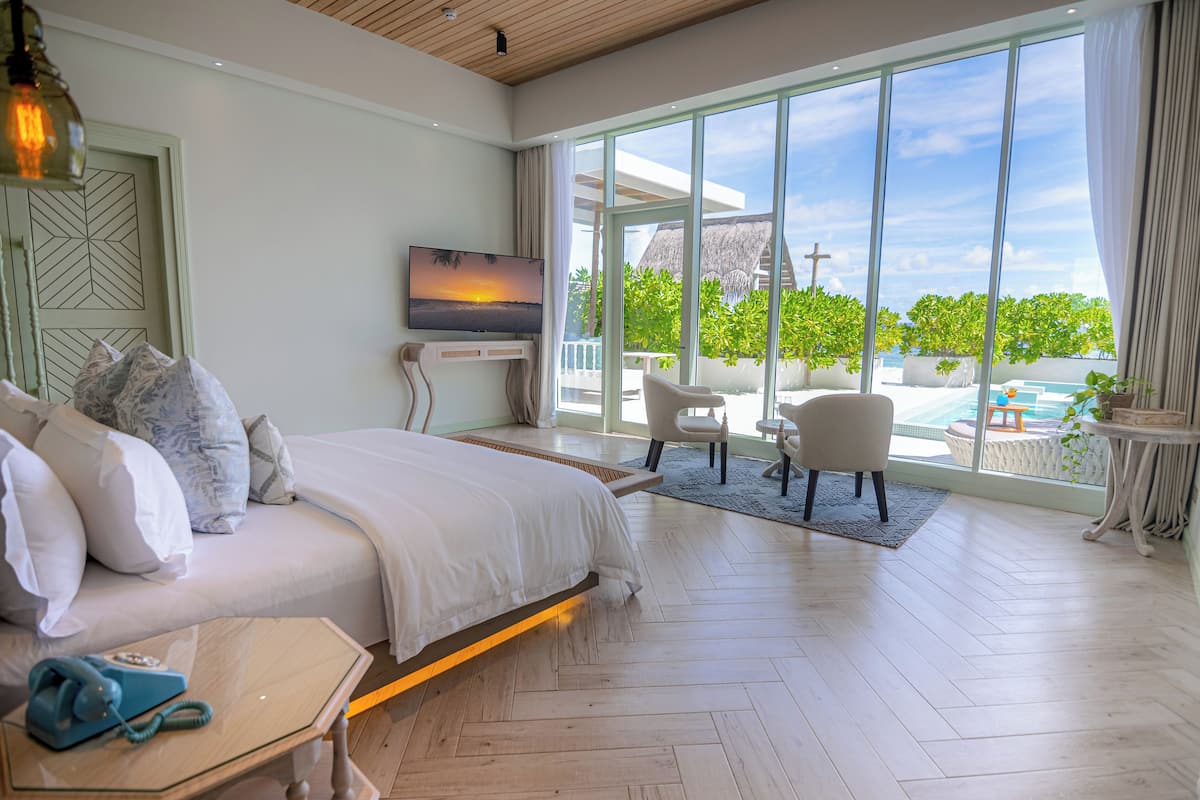 A spacious bedroom with a large bed, a TV, and a view of a pool and greenery.
