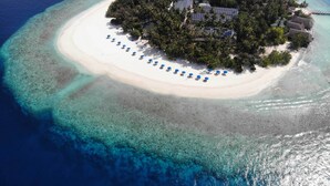Luchtbeeld van een tropisch eiland met een wit zandstrand, omgeven door helderblauw water en weelderige begroeiing. Er zijn verschillende zonnepanelen zichtbaar op het eiland, wat duidt op het gebruik van hernieuwbare energie.