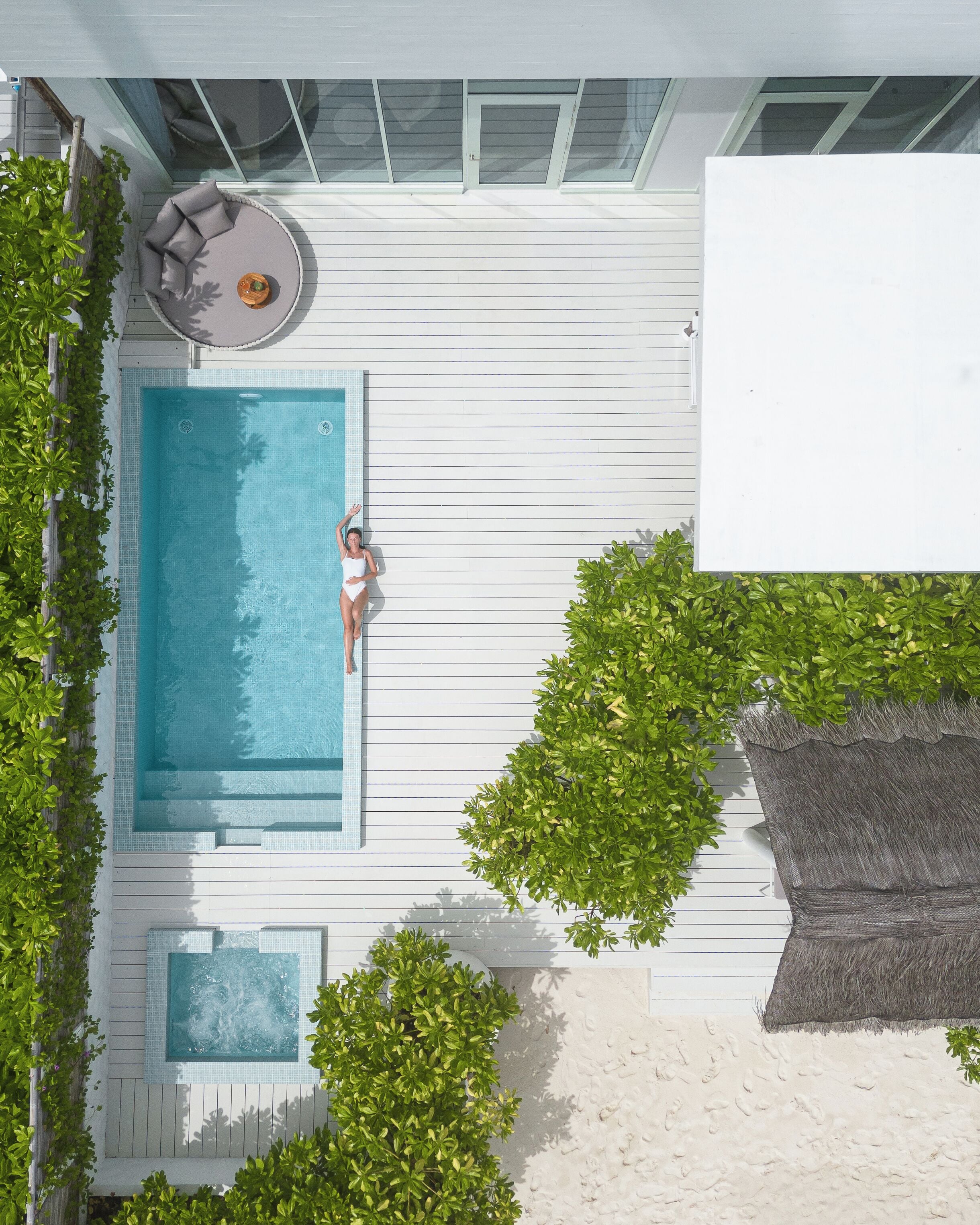 A rooftop pool with a person relaxing, surrounded by greenery and a modern architectural design.