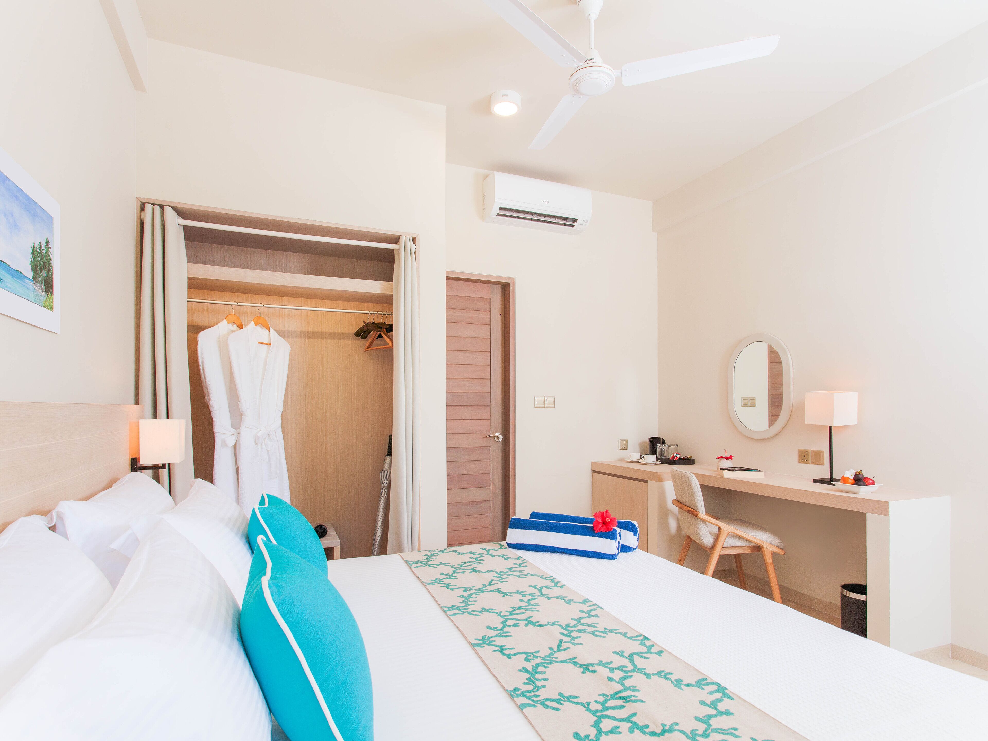 Habitación de hotel con cama, escritorio, silla, armario y ventilador de techo.