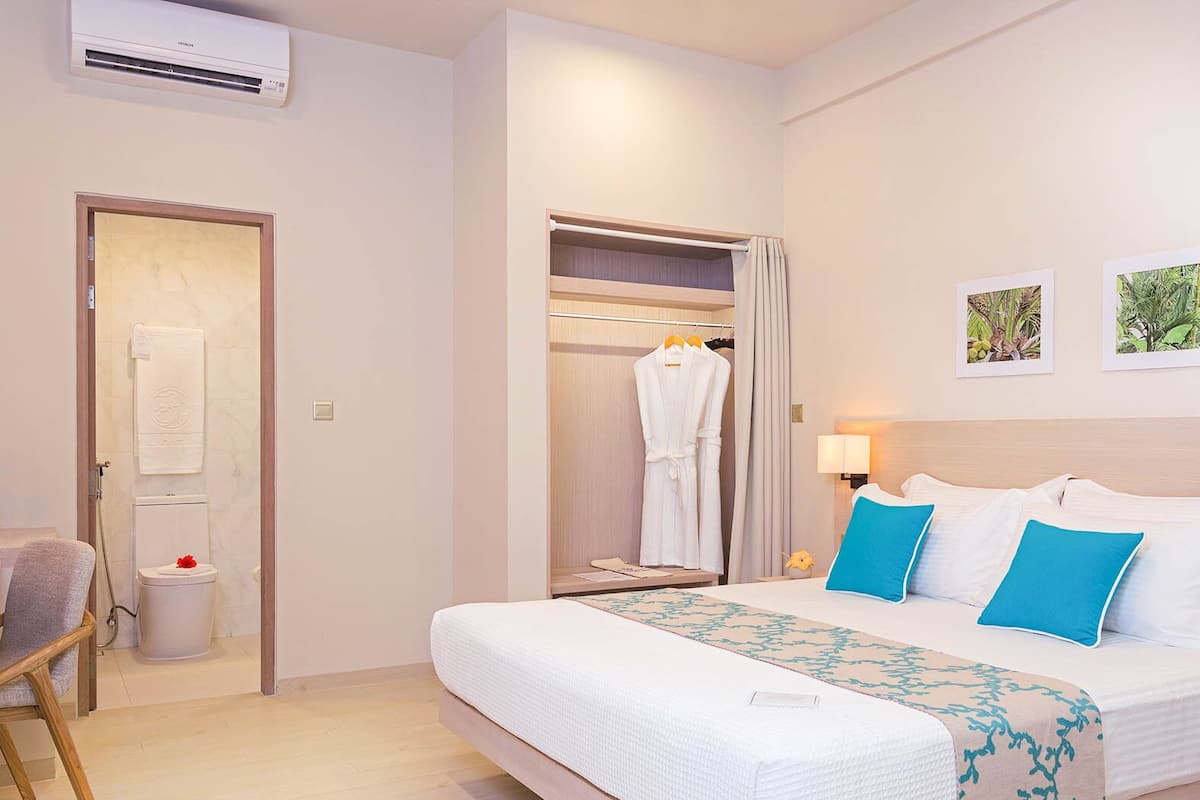 A hotel room with a bed, a robe, a towel, a chair, and a small table with a lamp.