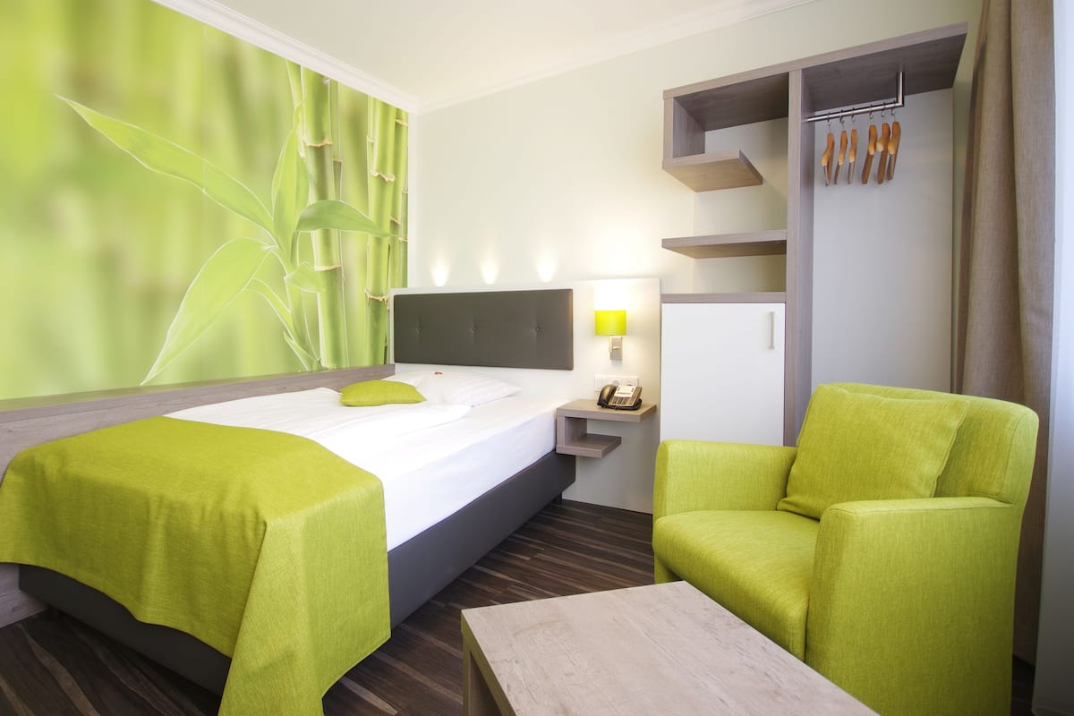 A hotel room with a bed, a desk, a chair, a lamp, and a wardrobe.
