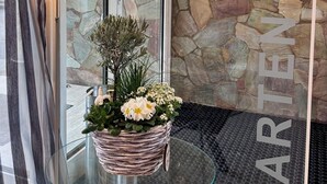 L’entrée d’un hôtel, avec un mur en pierre, une porte en verre, un panier en osier rempli de fleurs et une lampe.