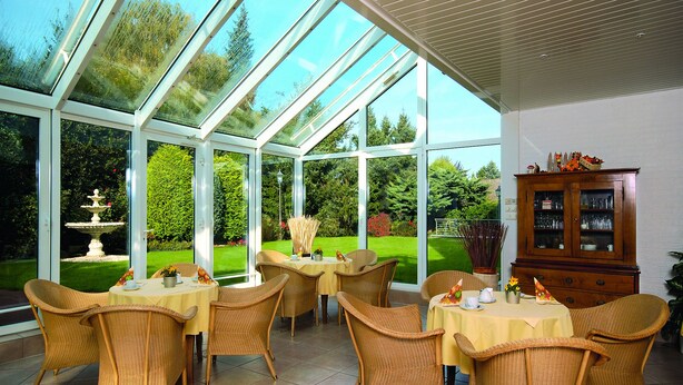 Une véranda aux murs de verre, meublée de mobilier en osier et dotée d’un buffet en bois.