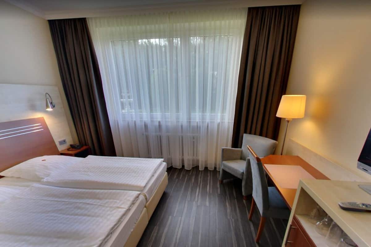 A hotel room with two beds, a desk, a chair, a TV, and a window with curtains.