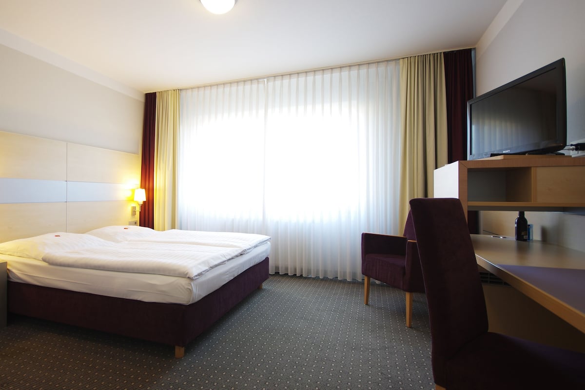 A hotel room with a bed, a desk, a chair, a television, and a window with curtains.