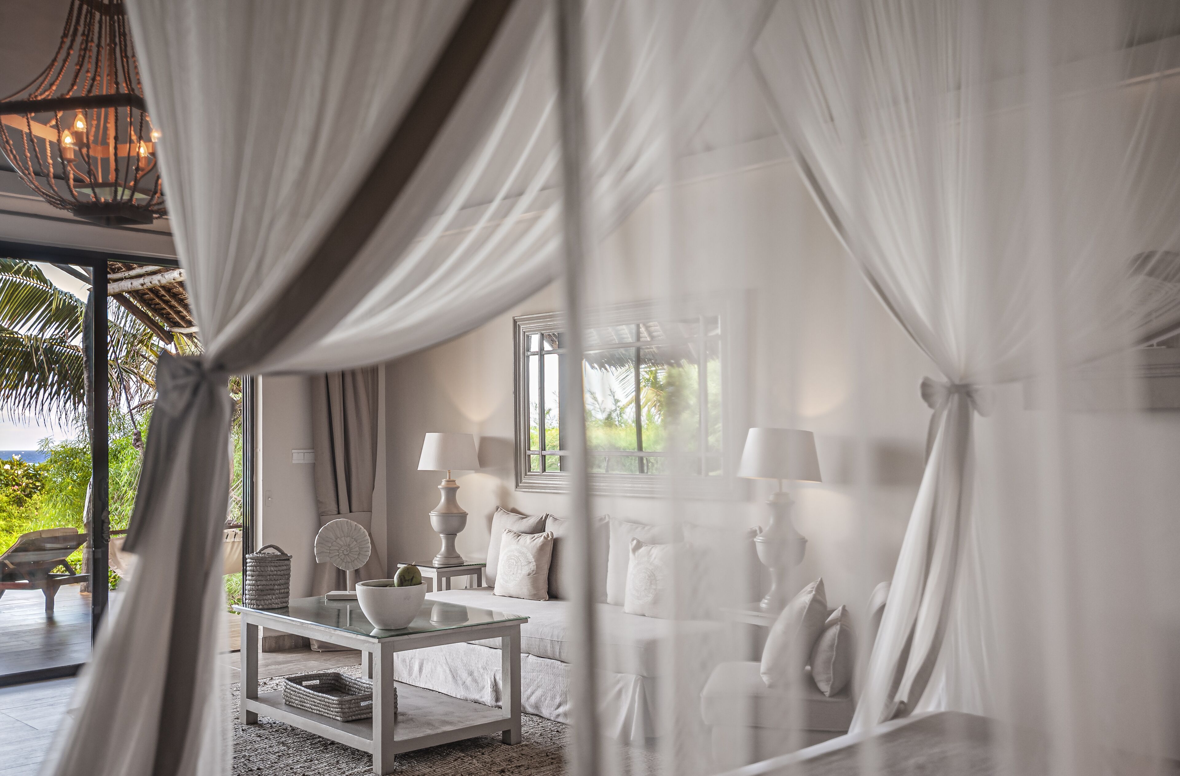 Une chambre avec un lit recouvert de rideaux blancs, une table de chevet avec des lampes et une vue sur la verdure à l’extérieur.