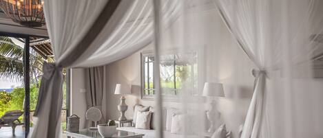 Une chambre avec un lit recouvert de rideaux blancs, une table de chevet avec des lampes et une vue sur la verdure à l’extérieur.