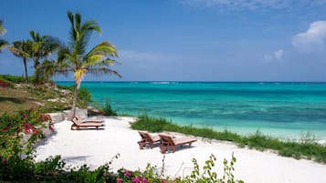 Een privéstrand, wit zand, ligstoelen aan het strand, parasols