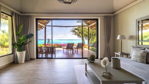 A room with a large sliding glass door leading to a balcony with a view of the ocean, a potted plant, a sofa, a lamp, and a table with decorative items. - Zawadi Hotel Zanzibar - All Inclusive (Dongwe)