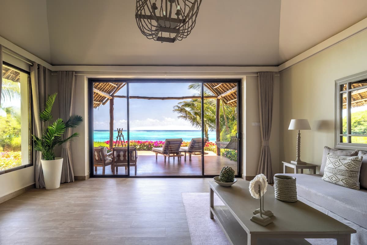 Habitación con un amplio ventanal corredero que da a un balcón con vista al océano, una planta en maceta, un sofá, una lámpara y una mesa con adornos.